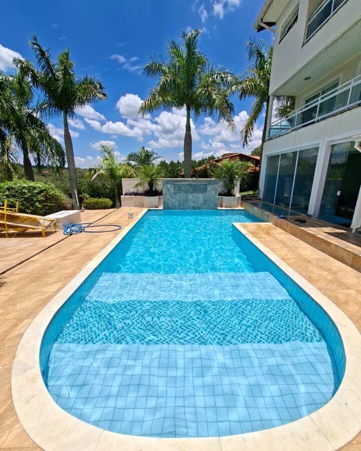 Piscina com água azul cristalina tratada pela LEPOOL, com palmeiras e casa ao fundo