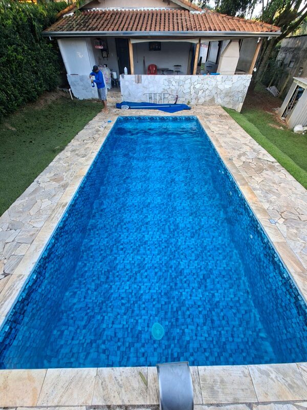 Piscina retangular de pastilha azul com casa ao fundo